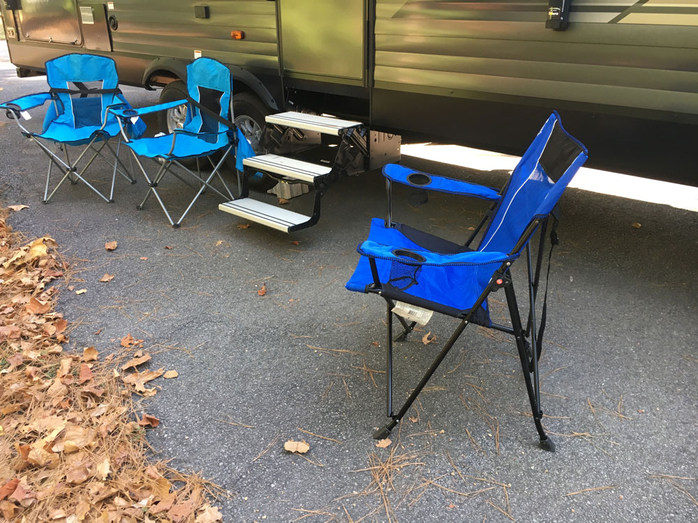 kijaro camping chair and regular bag chairs next to travel trailer