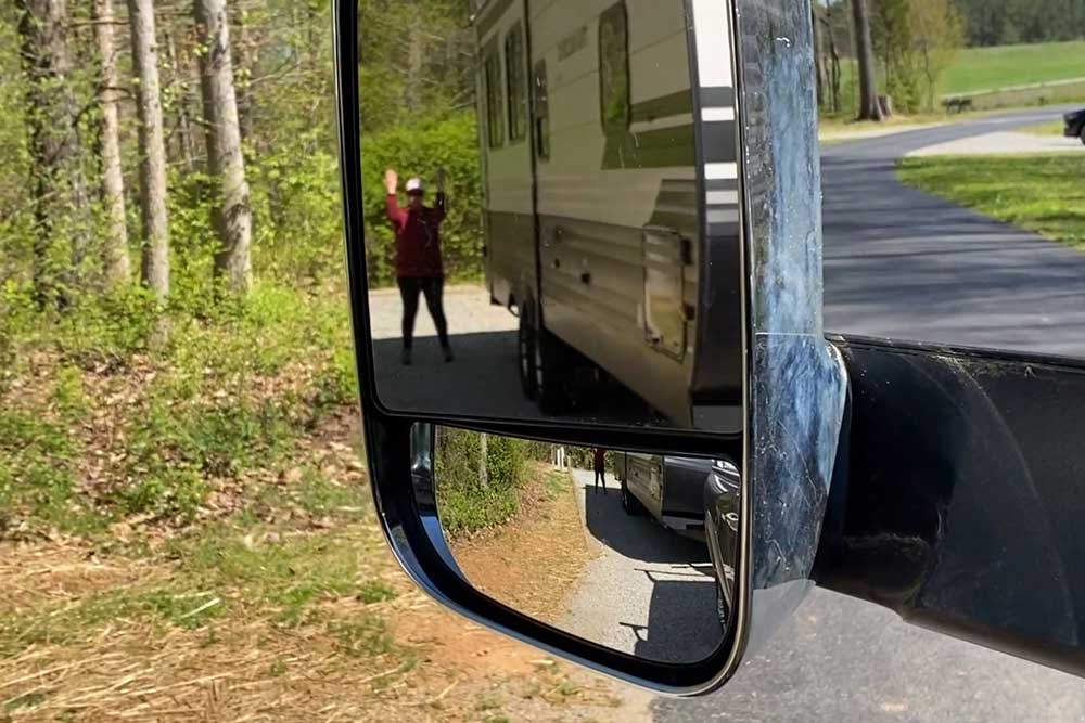 Spotter in truck mirror guiding RV backup into campsite